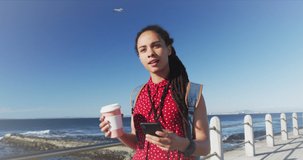 Animation of cup of coffee with percentage icon over biracial woman with coffee walking on promenade. health and fitness concept digitally generated video.