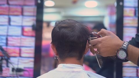 View from behind barber cuts man's hair with a clipper in a barbershop.