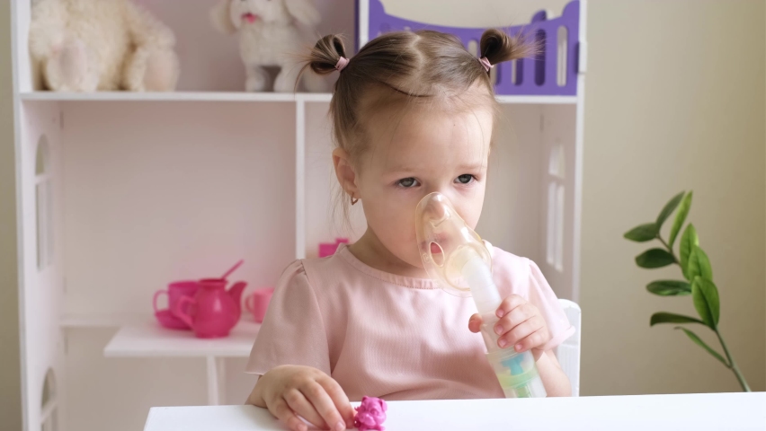 The child's health is very important. A calm, pretty girl is sitting at a table and inhaling vapors with medicine from an inhalation mask. Treatment of cough and asthma in children. Medical procedures Royalty-Free Stock Footage #1087889197