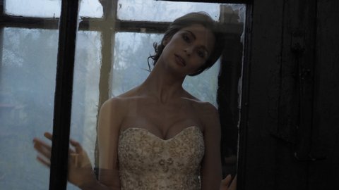 Woman in wedding dress poses behind glass on balcony