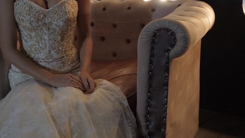 Brunette woman in bridal gown sits in armchair in studio