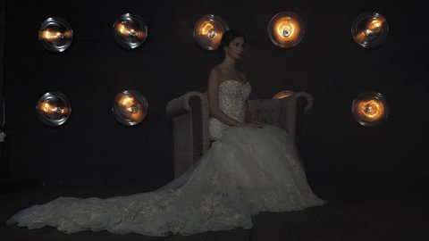Woman in bridal gown sits against illuminating spotlights