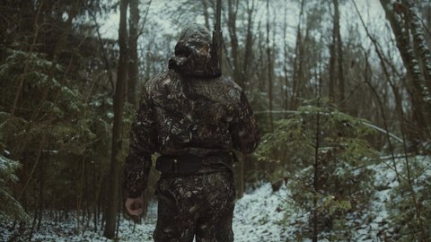 Back view of a hunter walking in the snow with a rifle and camouflage during hunting trip, winter hunting