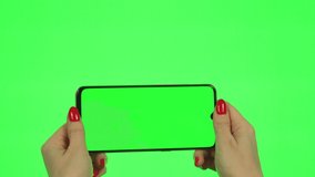 Glamorous Woman's Hand with Red Manicure Holds Smartphone Horizontally with Green Screen on Green Background, Alpha Channel, Chromakey, Mockup, Blank. Product Advertising, Video, Digital Device, PC.