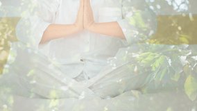Animation of leaves over caucasian woman practicing yoga and meditating. world meditation day and celebration concept digitally generated video.
