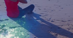 Animation of light spots over caucasian woman practicing yoga and meditating at beach. world meditation day and celebration concept digitally generated video.