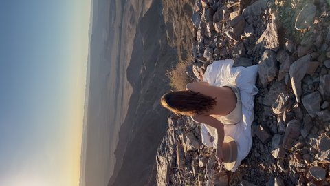 Vertical video. Young woman sitting topless on blanket at edge of Fish River Canyon in Namibia. Grand Canyon in USA. Rocky mountains, hiking. Travel in wild nature desert. Sunny summer day.