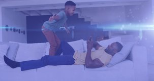 Animation of lights over happy african american father and son having fun on sofa. family, togetherness, spending quality time concept digitally generated video.