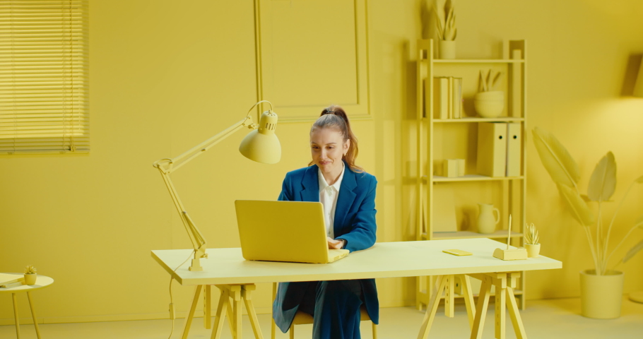 Slow motion of smiling businesswoman working with laptop on desk and celebrating her success by raising hands in the office with monochrome yellow color. Female worker expressing successful job Royalty-Free Stock Footage #1087908915