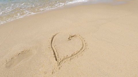 Sea waves covering heart drawn on beach sand. Symbol of romantic love on the beach. Concept of love, passion, relationships. Broken heart, suffering for love