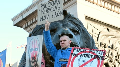 LONDON - FEBRUARY 27, 2022: Protester holds up anti Putin placards in front of Trafalgar Square Lion statue