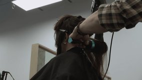 Stylist uses blow dryer and round brush to dry woman's long dark hair