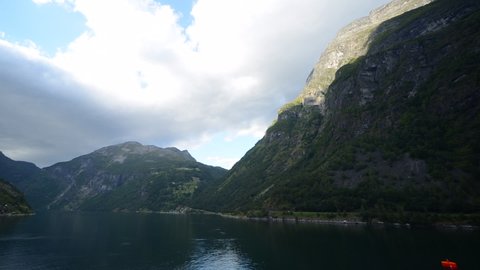 Unique time-lapse footage where the camera is placed in the front of a cruise ship, that is being undocked at the most famous fjord of Norway, Geirangerfjord. Cloud shadows are dancing on the hills.