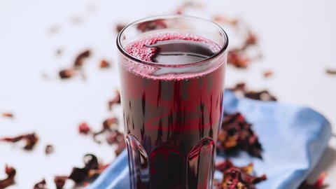 Hibiscus tea in a glass. Hibiscus leaves for making trendy tea. Red hibiscus tea on a blue napkin. Healthy food concept