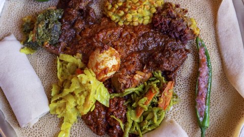 Zoom in on Injera served with chicken, egg, doro wat, berbere, vegetables and lentils. Injera, a traditional staple food of Ethiopia, is a sourdough flatbread made from teff flour.