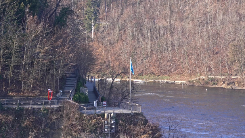 Rock with lookout point of famous Rhine Falls with Swiss flag and flag of Canton Zürich on a sunny spring day. Movie shot March 5th, 2022, Zurich, Switzerland.