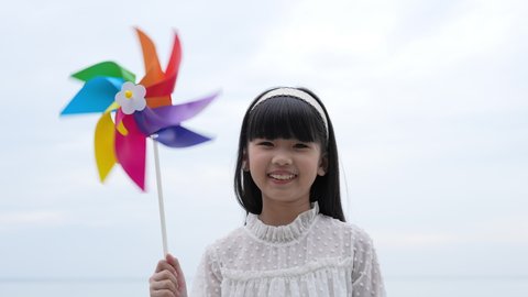 Holiday concept of 4k Resolution. Asian girl smiling happily on the beach. children playing with windmills. summer vacation travel.