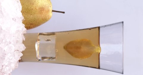 Sliced pears fall on the ice near a glass with pear juice on a white background. Slow motion, filmed on cinema camera, 8K downscale, horizontal frame, 4K.