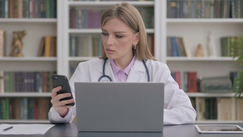 Lady Doctor using Smartphone while using Laptop in Clinic 