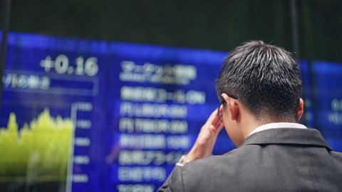 Depressed businessman in front of an electric bulletin board. Japanese translation: "yen","dollar","euro","pound"