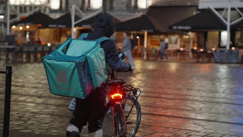 Ghent , Belgium - 02 18 2022: Deliveroo Rider Getting on his Electric Bike and Rides on the City Center Street To Deliver Orders for Clients and Customers - Following courier shot