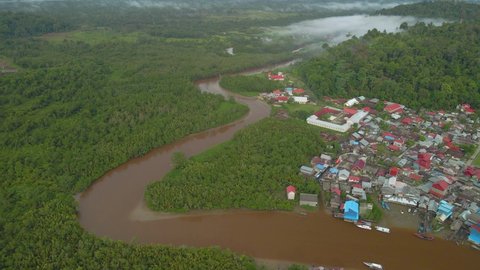 Indonesia, West Sumatra. Drone flying forward above river and Muara Siberut town, revealing hills, forest and mangrove.