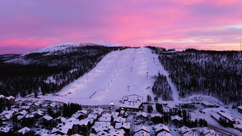 Levi , Finland - 02 24 2022: Aerial view of the Levi ski village and slopes, colorful winter dusk in Lapland - tracking, drone shot