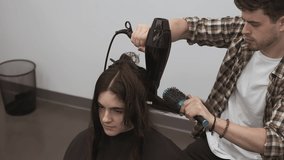 Young woman's long dark hair is blown dry by male stylist in salon