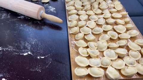 Homemade and handmade pelmeni. Russian national cuisine. It made from dough and beef meat with onion inside. Delicios healthy food. On the brown solid wood table with rolling pin. Metal forks 
