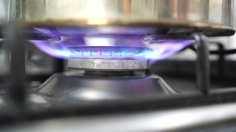 Unrecognizable woman hand turning on stove switch, lighting kitchen burner of gas stove indoors. Stove burner igniting into blue cooking flame. Natural gas inflammation. Close up, slow motion.