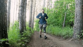 Disabled man with prosthetic limb with backpack walks through forest overcomes path and enjoys. Traveling on foot along forest road and active lifestyle for people with disabilities. active hiking - Powered by Shutterstock - Get 15% off with code: PIKWIZARD15