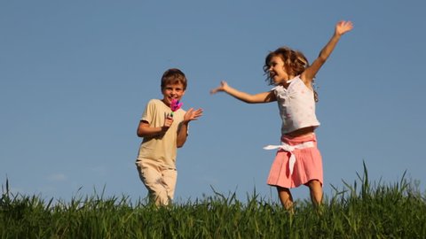 boy shakes rattle in form of colored hands, and his little sister dances cheerfully bouncing against blue sky