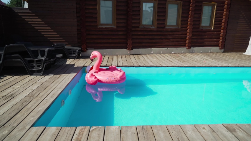 Inflatable swimming pink flamingo on the surface of the pool water outside.