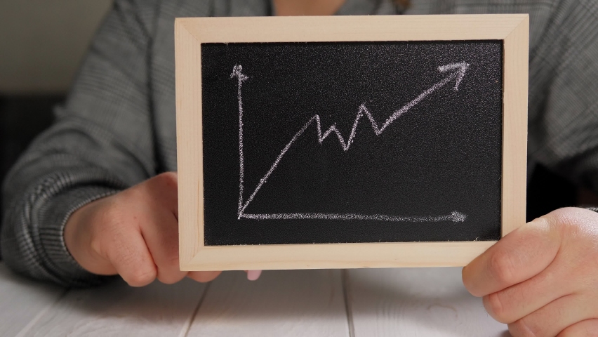 Close-up of a woman holding a gold bitcoin coin and a board with a graph of the growth of the price of a cryptocurrency. Finance and investment concept. BTC.