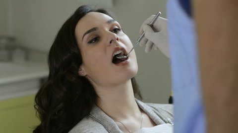 Portrait of a patient to the dentist for a check up and a dental cleaning. Dentist checks the teeth of a young woman with a mirror. Portrait of a woman smiling after visiting orthodontist.
