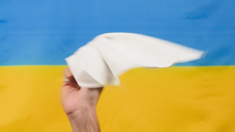 hand waving white kerchief with ukrainian flag in background