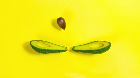4k Avocado is split into two halves. Halves throw a bone to each other, as if playing tennis. Looped video. Concept of proper nutrition and healthy fruits. Yellow background. Stop motion animation.