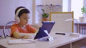 Home online learning. A boy in white headphones watches an online lesson