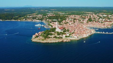 Rovinj with Church of St. Euphemia surrounded by blue Adriatic sea and lush forests. Traditional architecture of old Croatian town. Panorama view