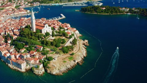 Old city Rovinj on coast of Adriatic sea near small island on sunny summer day. Church of St. Euphemia surrounded by lush trees. Aerial view