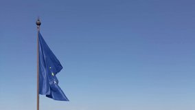 Footage of the European flag of the EU fluttering in the wind on a bright sunny day against a clear blue sky.