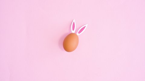 6k Creative Easter egg with rabbit ears appear and move on pastel pink background. Flat lay stop motion
