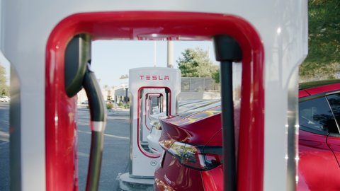 Los Angeles, California USA, March 2022. White and red Tesla autonomous electric cars refilling energy at free of charge super fast charging station on parking lot. Luxury EV vehicles charging battery