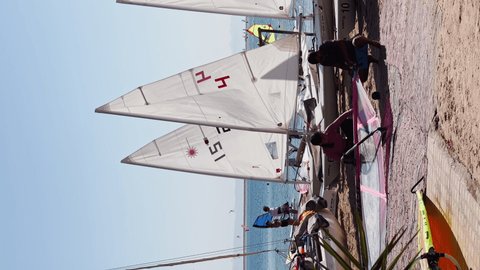 Egypt, Dahab, 10 November 2021: Young guys prepare dinghies for going to sea in sunny weather, small sailboats on the beach, a sports competition, sails and masts, a lot of vacationers on the beach