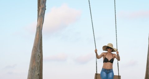Woman with swinging free. A woman in a good mood swinging on the wooden handmade swing on the beach.