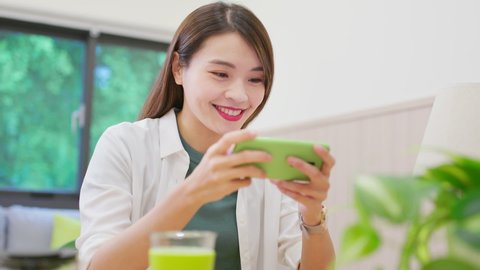 asian young woman is playing and winning mobile games happily with fist gesture at home