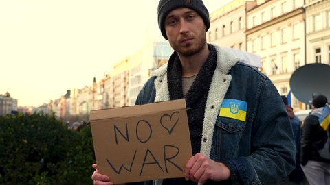 Man with antiwar protest sign and Ukraine flag at a rally in Prague.