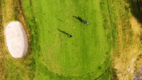 Golfer hits ball rolling towards flagstick on putting green, Molndal near Gothenburg in Sweden. Aerial top-down rising