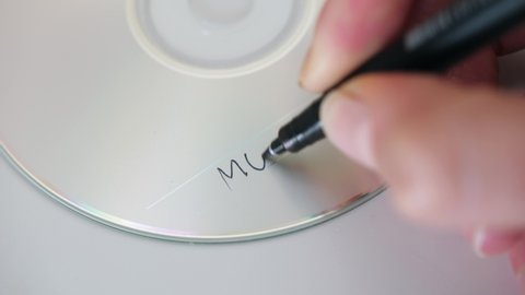 woman hand writing word music with pen on cd, closeup static shot on white surface