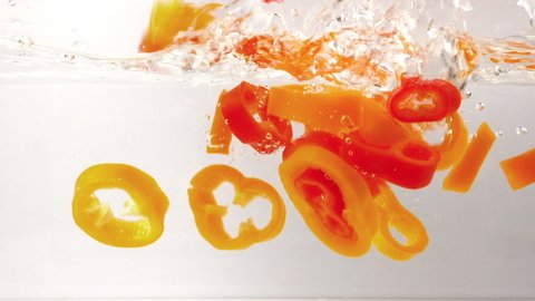 sliced organic bell peppers falling and splashing into fresh water, in slow motion